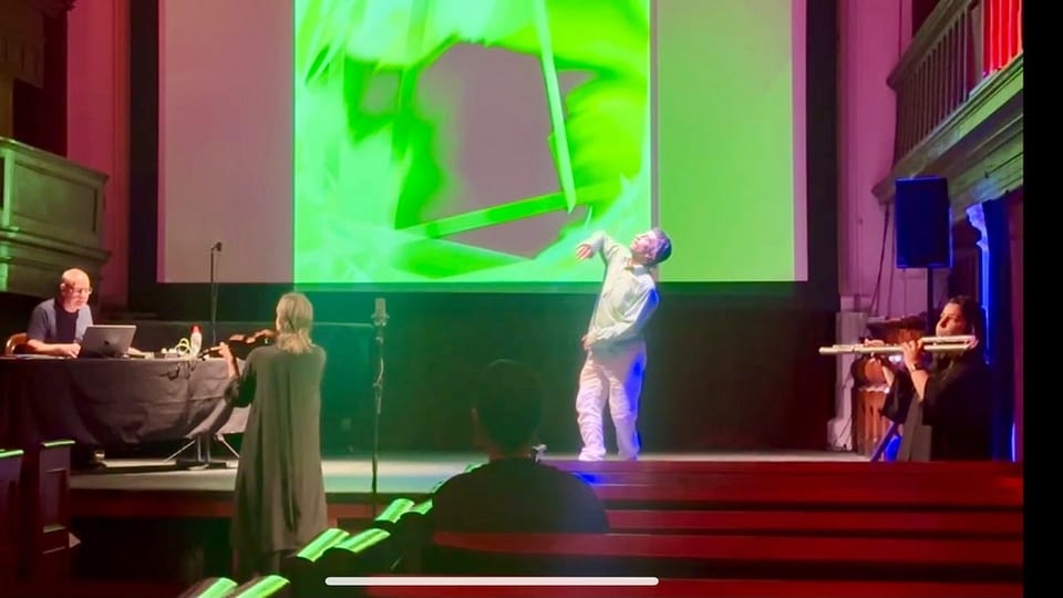 A dancer in front of a large green projected drawing at Triskel Arts Centre, Cork. A violinist and a flautist play nearby, and Steve Meyfroidt works at a laptop at the side of the stage.